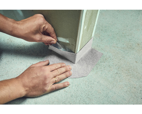 Gedetailleerde weergave van het aanbrengen van een afdichtband op de voet van de muur binnenshuis