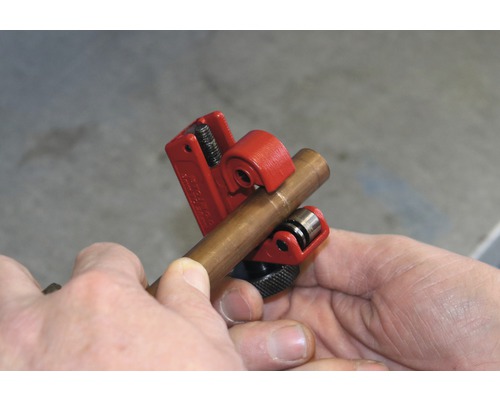 Een koperen pijpsnijder snijdt een koperen pijp.