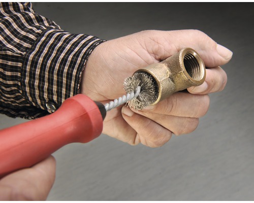 Een persoon reinigt een messing buisfitting met een draadborstel.