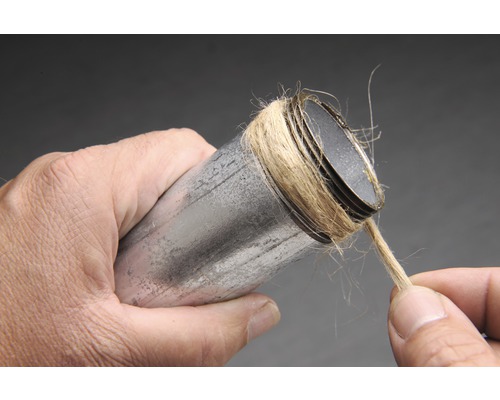 Een man wikkelt hennep om een metalen pijp om deze af te dichten.