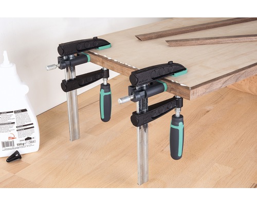 Op de afbeelding zijn twee lijmklemmen te zien die een houten plank vastklemmen, voorzien van houten latten en lijm.