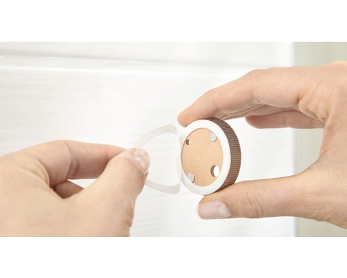 Een hand houdt een ronde magnetische slotbevestiging vast en verwijdert de beschermfolie van de plakstrip.