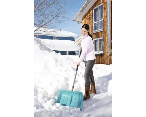 Vrouw schept sneeuw met een sneeuwschuiver voor een huis.