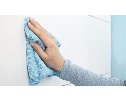 Een hand veegt een wit oppervlak schoon met een microvezeldoek