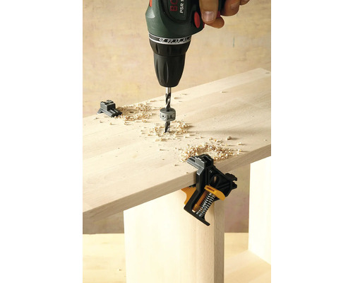 Een boormachine boort in een houten plank, bevestigd met een hoekklem.