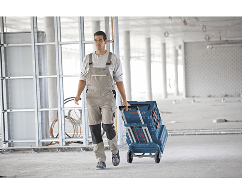 Ambachtsman trekt een gereedschapskoffer met wielen van het merk Bosch over een betonnen vloer in een casco.