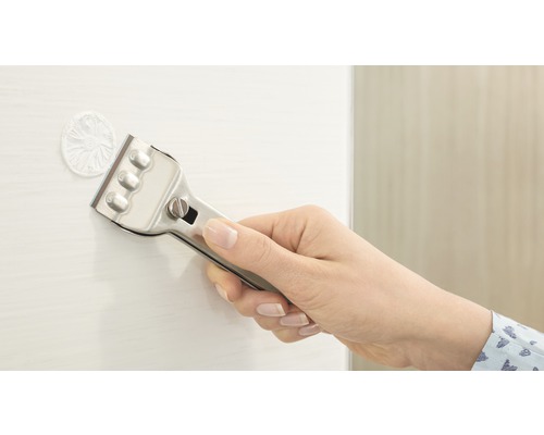 Een hand houdt een glasschraper vast om resten van een oppervlak te verwijderen.