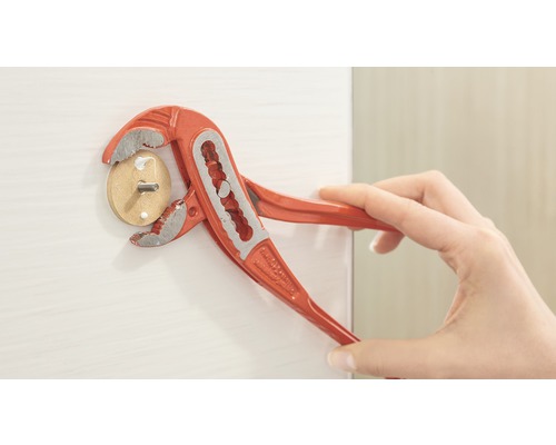 Een persoon gebruikt een waterpomptang om een houten deuvel met schroef in een wit oppervlak te draaien.