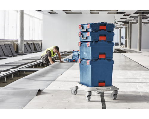 Stapelbare gereedschapskoffers op een rolplank op een bouwplaats met een werknemer
