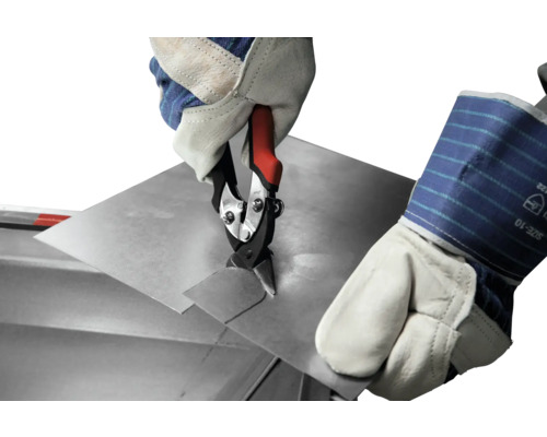 Een hand met beschermende handschoen knipt een plaat met een plaatschaar.