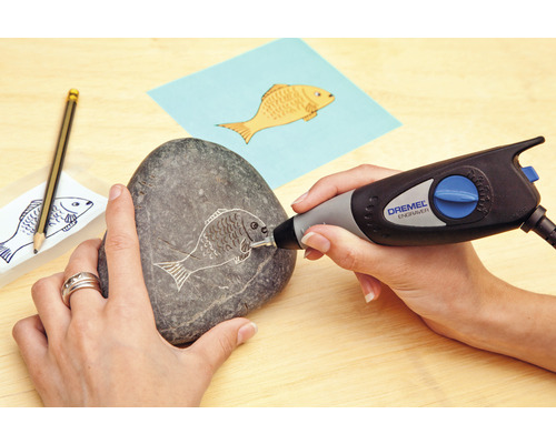 Een persoon graveert een vismotief in een steen met een Dremel graveermachine.