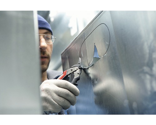 Een man knipt met een blikschaar een gat in een metalen plaat.