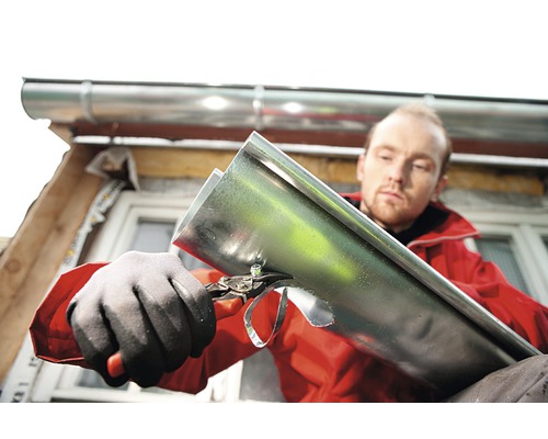 Man knipt dakgoot met een blikschaar