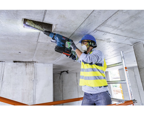 Een bouwvakker boort met een boorhamer een gat in een betonnen plafond.