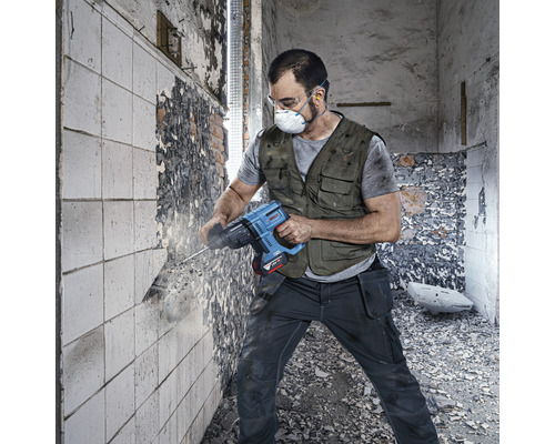 Ambachtsman met veiligheidsmasker en veiligheidsbril werkt met een sloophamer aan een muur.