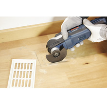 Oscillerend multifunctioneel gereedschap in gebruik voor het snijden van hout naast een ventilatierooster