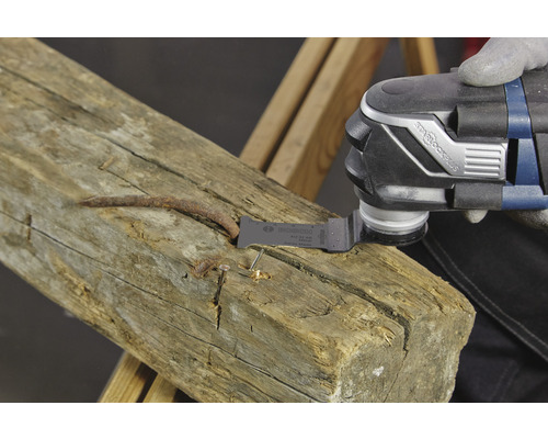 Een oscillerende multitool zaagt een spijker uit een stuk hout.