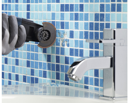 Een arbeider met handschoenen verwijdert tegels met een multifunctioneel gereedschap in een badkamer