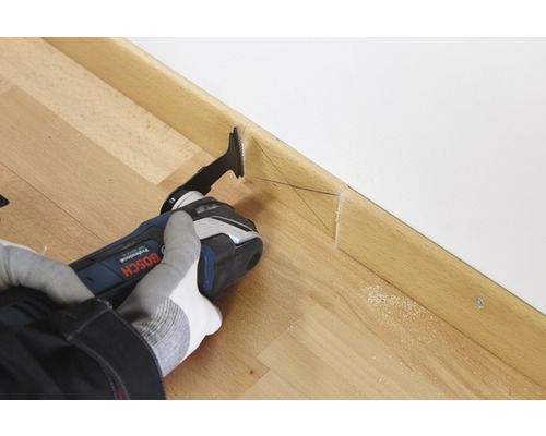 Iemand snijdt een houten plint met een multifunctioneel gereedschap.