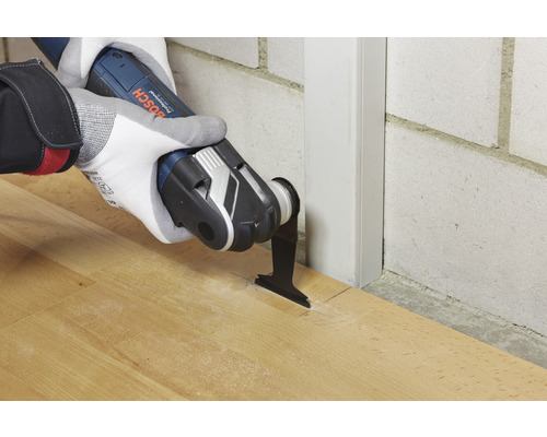 Oscillerend multifunctioneel gereedschap in gebruik op een houten vloer naast een wandlijst.