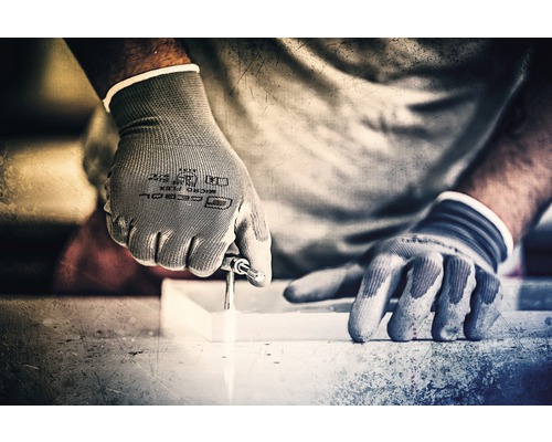 Een persoon boort met handschoenen een gat in een werkstuk.