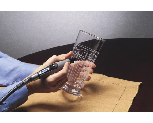 Een persoon graveert met een graveerapparaat een glas met een lijnenpatroon.