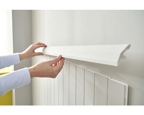 Persoon monteert een witte sierlijst op een wand met lambrisering
