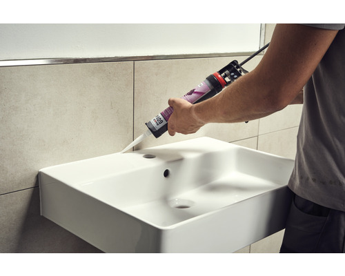 Een vakman dicht een wastafel af met siliconen.
