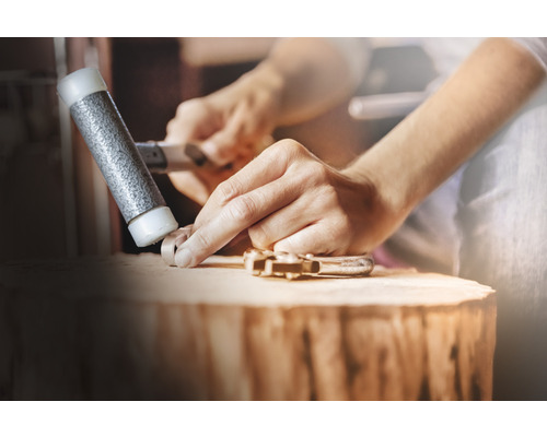 Man vormt een werkstuk met een hamer op een houten blok.