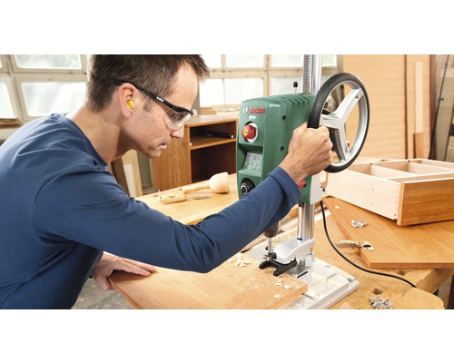 Een man bedient een tafelboormachine in een werkplaats.