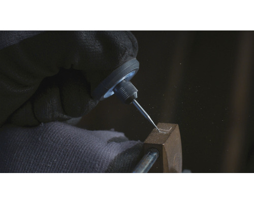 Gedetailleerde opname van een hand met beschermende handschoen, die met een graveernaald een vorm graveert in een metalen object