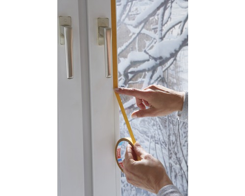 Een persoon dicht een raam af met afdichtband.