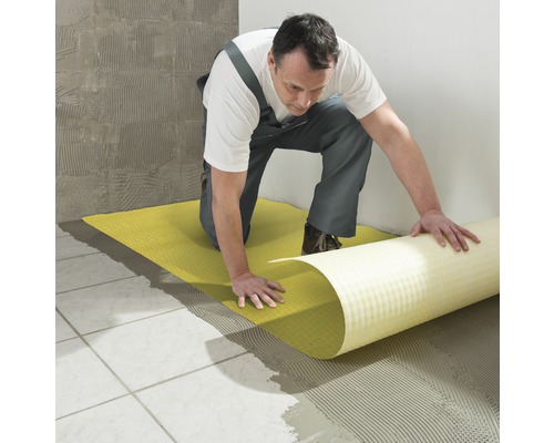 Een man legt een ontkoppelingsmat op een betegelde vloer om een vlak oppervlak te creëren voor verdere tegelwerkzaamheden.