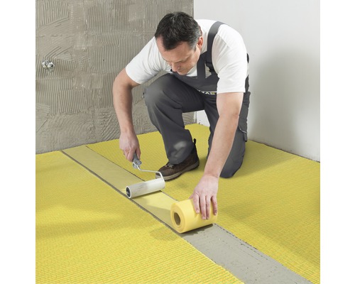 Ambachtsman legt ontkoppelingsmat met verfroller in de badkamer.