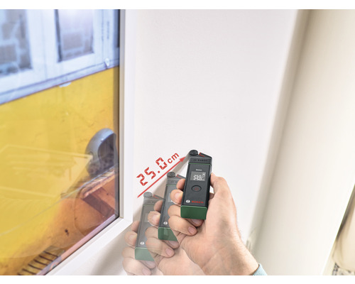 Hand houdt elektronisch meetapparaat tegen een muur, dat een afstand van 25,0 cm aangeeft