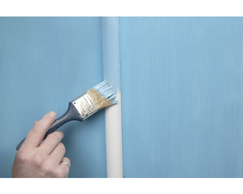 Een persoon schildert een pijp met een kwast en verf.