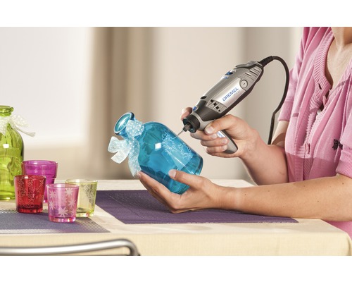 Vrouw graveert een blauw glas met een Dremel multi-tool. Decoratief glaswerk op de achtergrond.