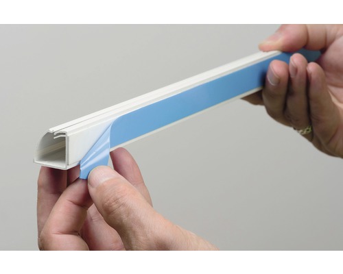 Persoon verwijdert de beschermfolie van een zelfklevend kabelkanaal.