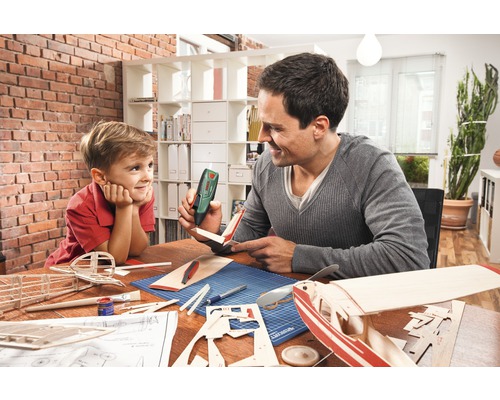Vader en zoon bouwen samen een modelvliegtuig met een lijmpistool aan een tafel.
