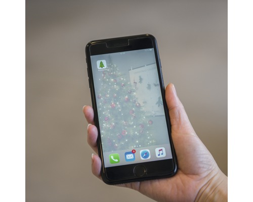 Een mobiele telefoon wordt vastgehouden en toont de Hornbach app met een kerstboom op de achtergrond.