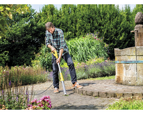 Man verwijdert onkruid met een elektrische voegenkrabber op een betegeld oppervlak in de tuin.
