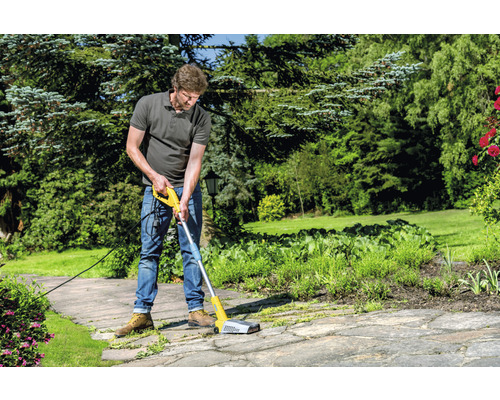 Man gebruikt een elektrische voegenborstel voor het reinigen van bestrating in de tuin.