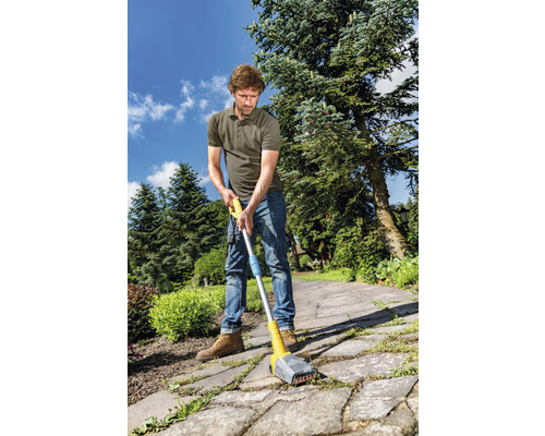 Een man gebruikt een voegenreiniger op een verhard pad in de tuin om onkruid te verwijderen.