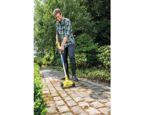 Een man gebruikt een elektrische voegenborstel om een verhard pad in de tuin schoon te maken.