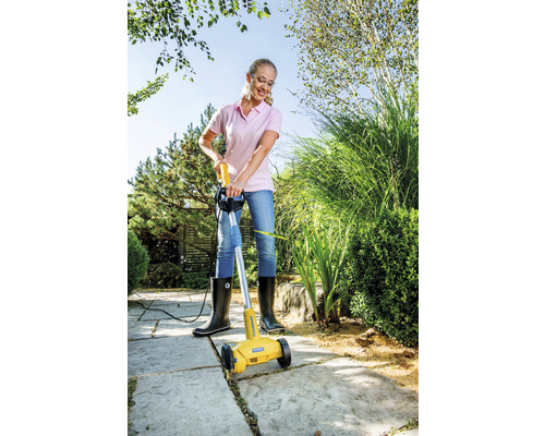 Een vrouw gebruikt een elektrische voegenreiniger om onkruid tussen tegels te verwijderen.