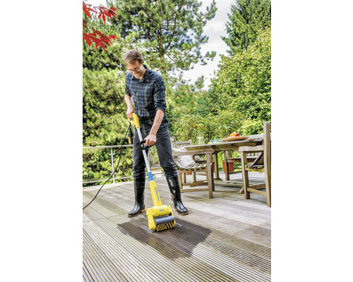 Man reinigt een houten terras met een terrasreiniger.
