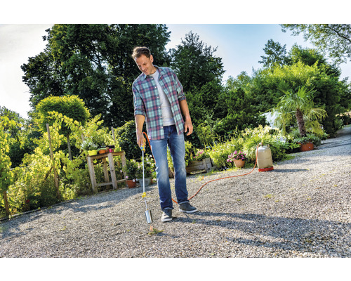 Een man gebruikt een gasbrander om onkruid te bestrijden in de tuin.