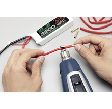 Een persoon gebruikt een heteluchtpistool om een connector aan een kabel te bevestigen. Een SLS batterij is op de achtergrond te zien.