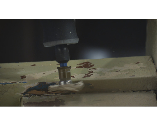 Een boormachine schuurt verf van een raamkozijn.