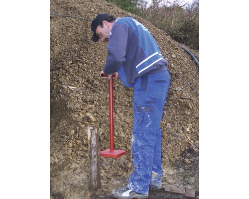 Een man slaat een houten paal in de grond met een grondstamper.